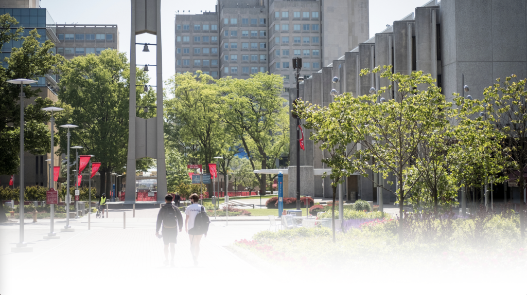 students walking on pathway towards bell tower, surrounded by campus buildings