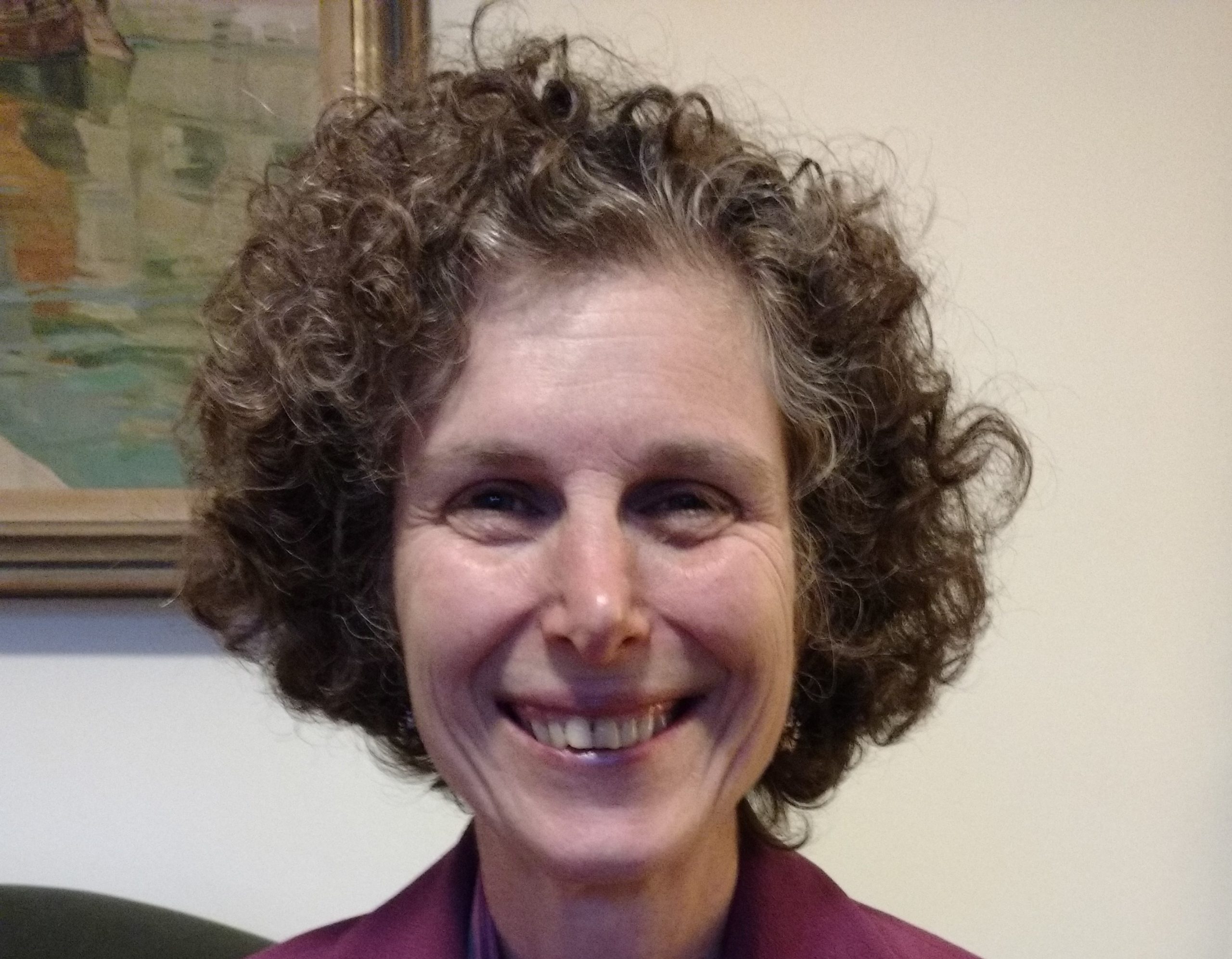 Photo of the author. White woman, medium length curly brown hair, staring directly at the camera and smiling broadly.
