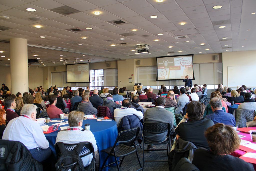 large conference room with tables filled with conference attendees and Tom Tobin at the front of the room