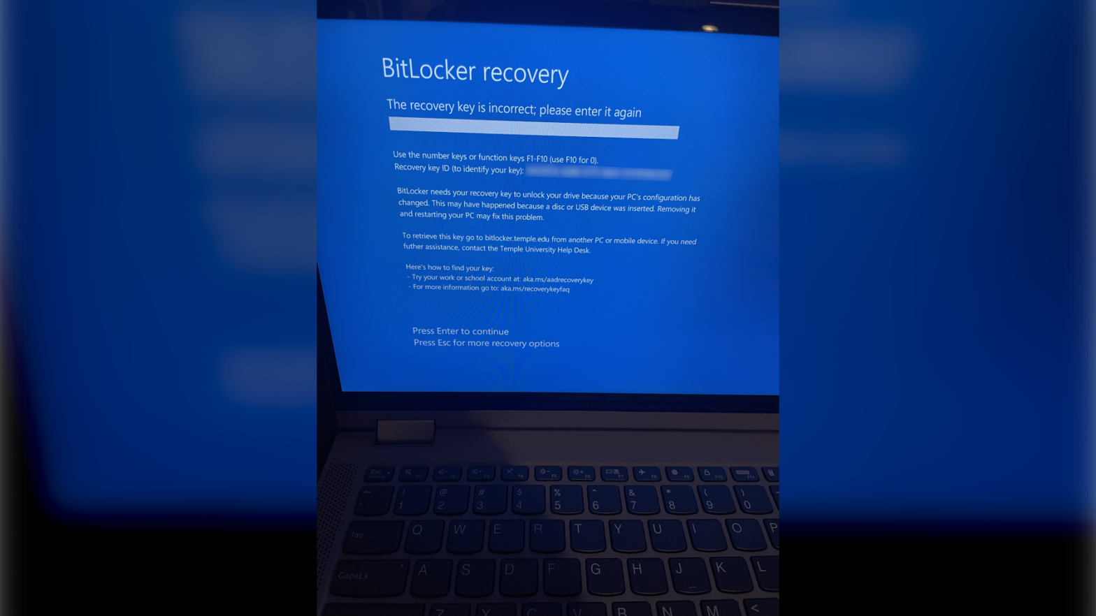 A photo of a laptop with an error screen titled "BitLocker Recovery"