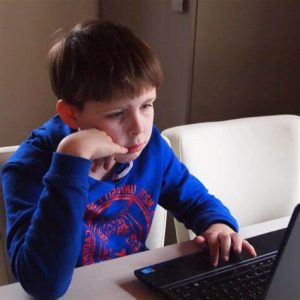 School-aged boy uses laptop computer, leaning cheek against his hand.
