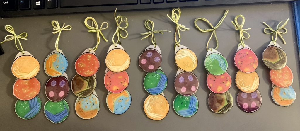 Shrink plastic colored pencil drawings of various bacteria grown on differential agars made into ornaments