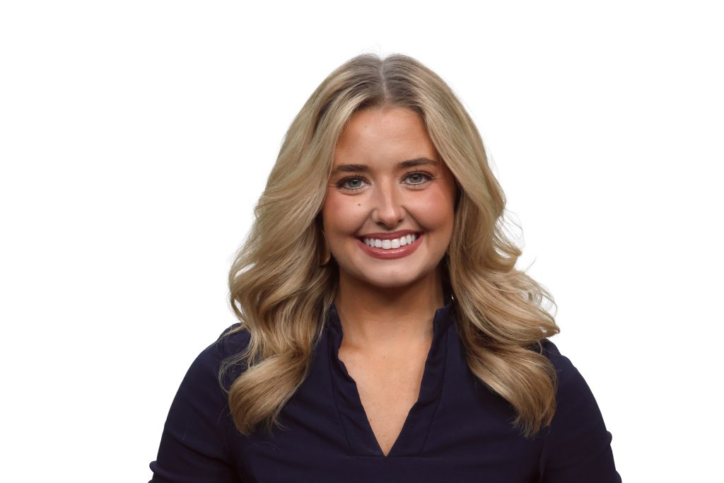 Professional headshot of Lindsey Moppert, a smiling young woman with long wavy blonde hair, wearing a navy v-neck top against a white background