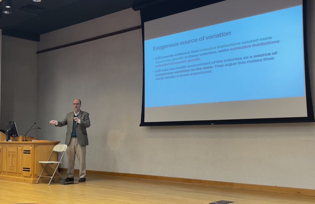 Professor Dimitrios Diamantaras lecturing, in front of a slide display