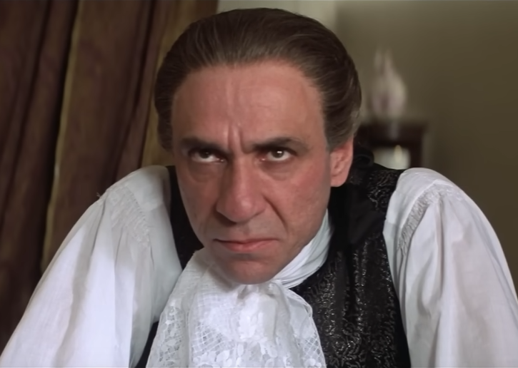 Screenshot of F. Murray Abraham as Antonio Salieri in Amadeus. Salieri, in a medium close-up, glares malevolently while thinking (possibly) murderous thoughts about Mozart. 