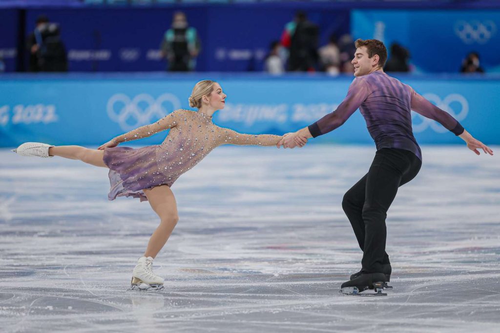 A male and female figure skating pair wearing purple and black costumes strike a pose during their routine.