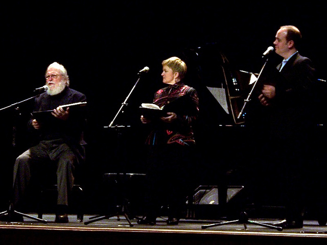 Three people in concert attire on stage, performing.