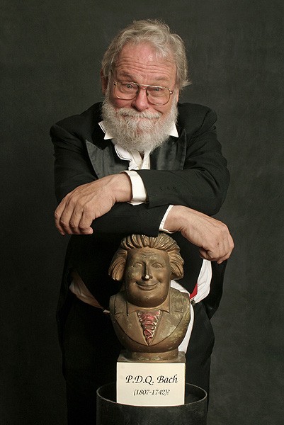Elderly man with a white beard, spectacles, and a cheeky grin, wearing a tuxedo and leaning with arms crossed against a comical bust titled "P.D.Q. Bach (1807-1742)?"