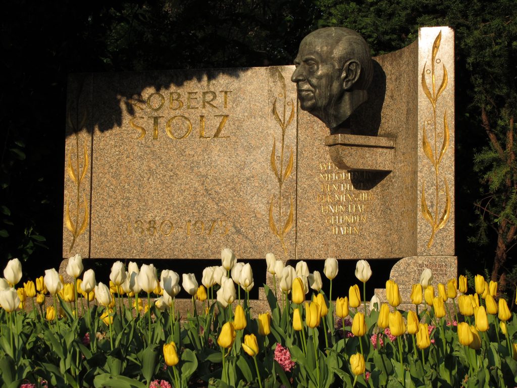 A decorative headstone reading "Robert Stolz" and decorated with a large bust, surrounded by tulips.
